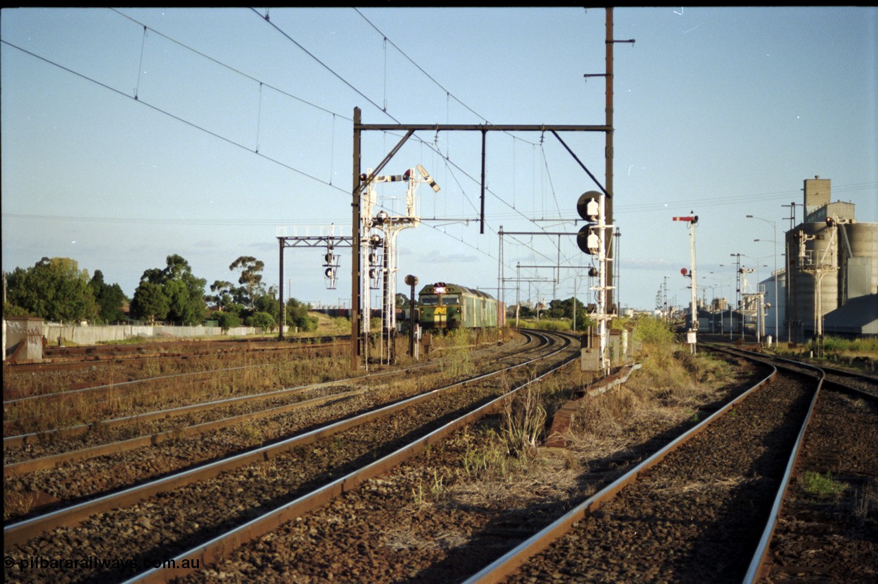 124-18
Sunshine looking from the passenger lines across to the Independent Through Goods lines, signal post 71 at camera, disc and semaphore signal posts 31 and 31B for control of the Independent Trough Goods lines, 31B pulled off for down Adelaide broad gauge goods train to cross over the passenger lines, BL classes Clyde Engineering EMD model JT26C-2SS serial 83-1014 and BL 35 Clyde Engineering EMD model JT26C-2SS serial 83-1019 in AN livery, standard gauge Sunshine Loop to the left of train, Newport Loop Line and GEB sidings at far right.
Keywords: BL-class;BL30;Clyde-Engineering-Rosewater-SA;EMD;JT26C-2SS;83-1014;