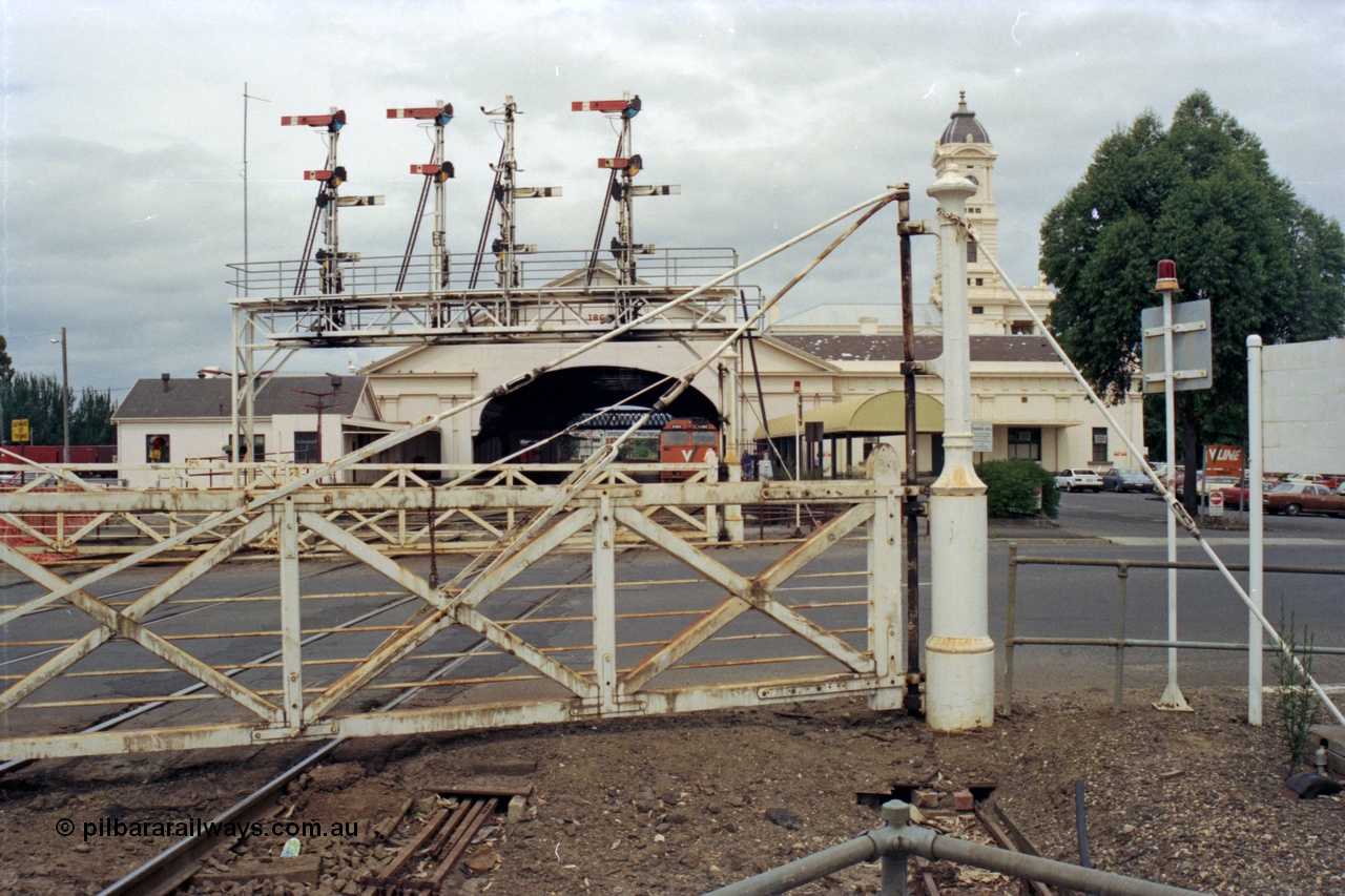 128-13
Ballarat Station, Lydiard St or B signal box, view across Lydiard Street grade crossing, interlocked gates, signal gantry with semaphore signal posts 26 to 29, looking east, V/Line N class N 464 'City of Geelong' Clyde Engineering EMD model JT22HC-2 serial 86-1193 at station, station building and canopy, point rodding under road.
Keywords: N-class;N464;Clyde-Engineering-Somerton-Victoria;EMD;JT22HC-2;86-1193;