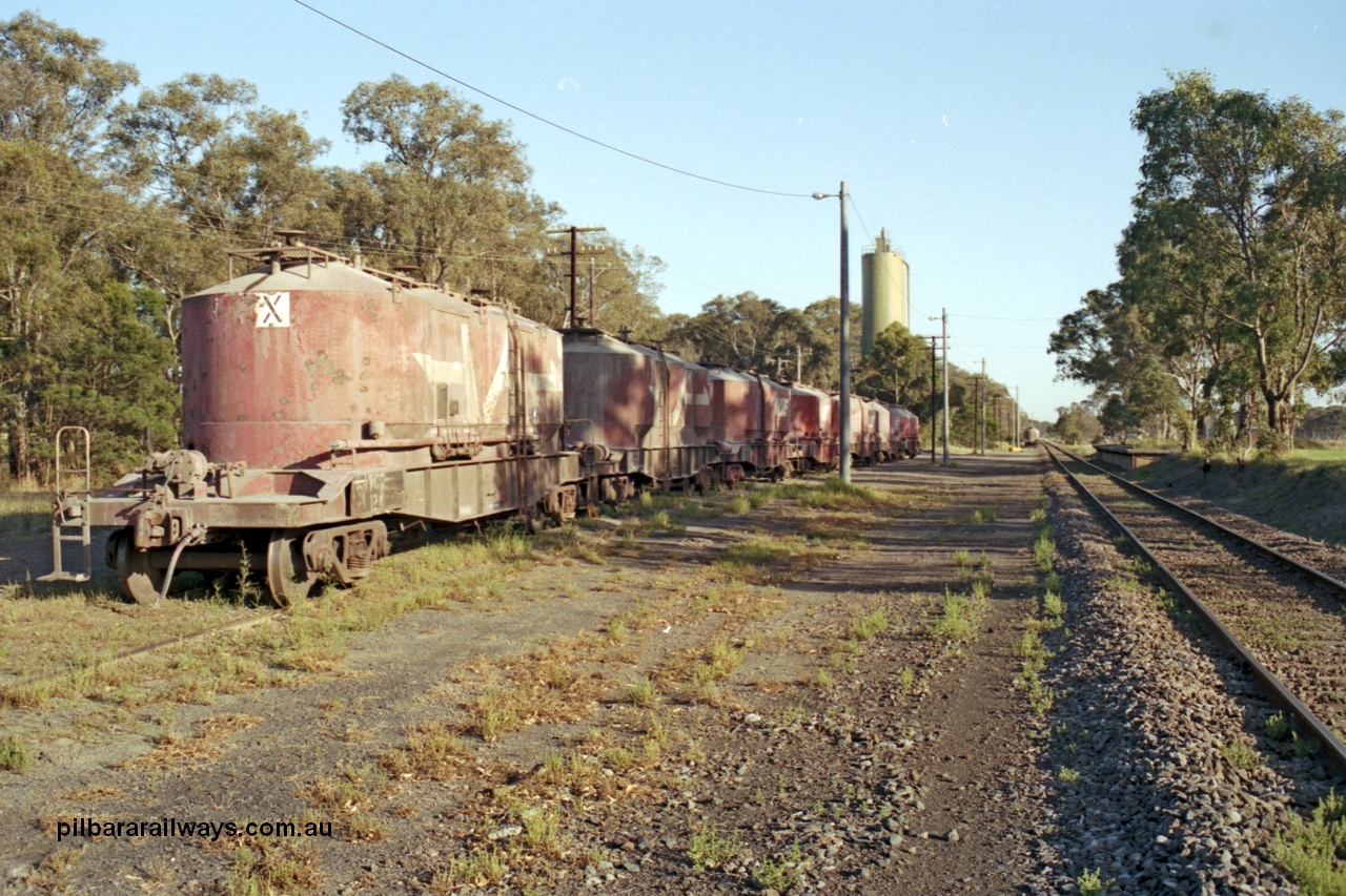 129-1-15
Lyndhurst, station overview, V/Line VPCX type bogie cement waggons in rakes, platform on RHS, looking towards Melbourne, Blue Circle Cement plant in the background. Location is [url=https://goo.gl/maps/4zF5DDSnJN6R9cKe8]Geo Data[/url].
Keywords: VPCX-type;