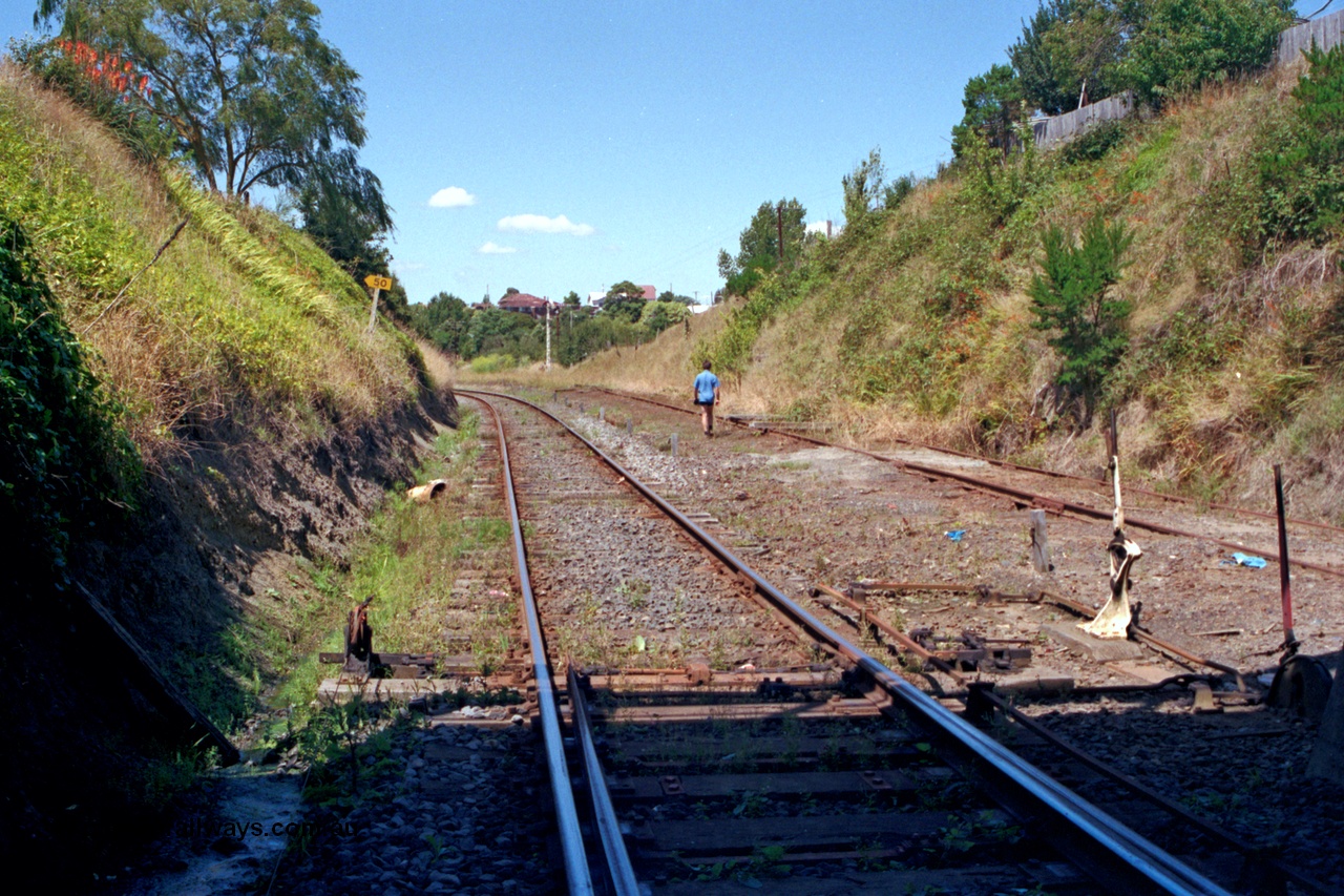 129-2-17
Korumburra track view, looking in the down direction from underneath Bridge Street, former Outtrim - Coal Creek line with baulks on right, Port Albert - Yarram line curving around to the left, points, points and signal lever with interlocking and rodding.

