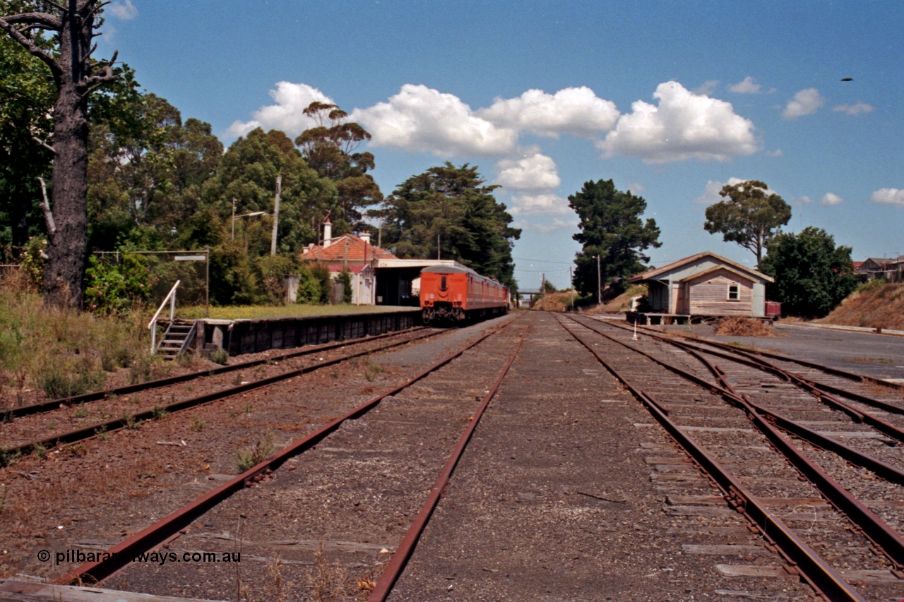 129-2-31
Leongatha station overview, looking east, stabled passenger train H set at platform, goods shed on right.
