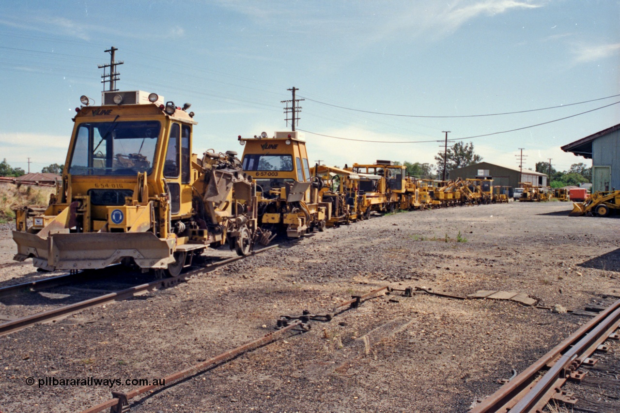 137-1-13
Euroa, V/Line broad gauge track re-surfacing gang's tack machines are stabled on No.5 Rd, ballast regulators, tampers and sleeper inserting machines make up this motley collection, the goods shed is at right of frame.
