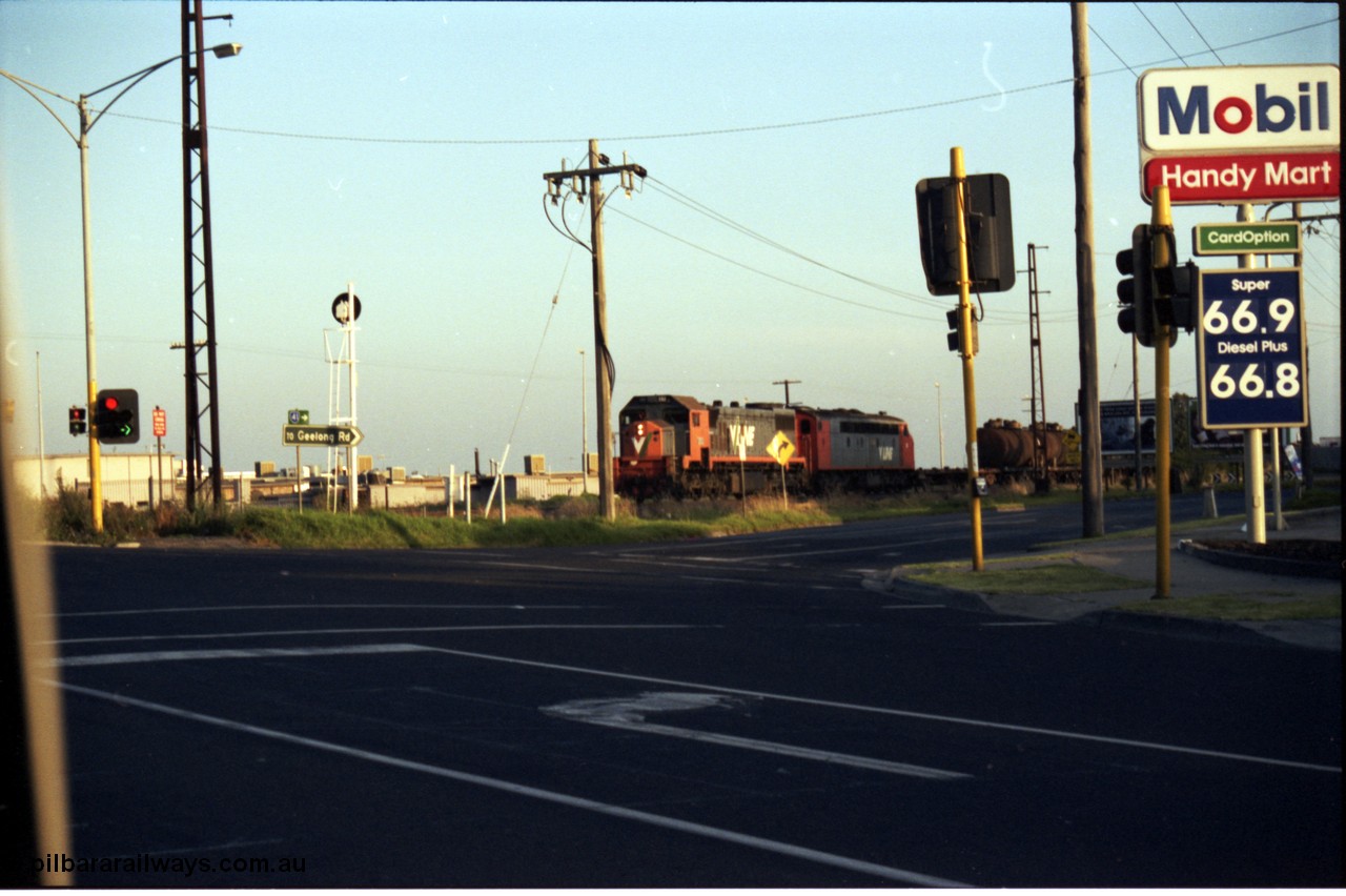 141-1-15
Sunshine, Wright Street / Sunshine Road grade crossing, 66 cents a litre for fuel?? Must have been 1992, and broad gauge V/Line X class and S class with the down Corio - Wodonga oil (fuel) train.
Keywords: X-class;Clyde-Engineering-Granville-NSW;EMD;G26C;