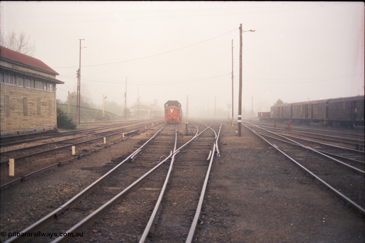 142-1-13
Benalla yard view, stabled broad gauge Wodonga goods train 9303 with V/Line X class X 48 Clyde Engineering EMD model G26C serial 75-795, Benalla signal box, station in background, very foggy, NSW louvre vans at right, track view.
Keywords: X-class;X48;Clyde-Engineering-Rosewater-SA;EMD;G26C;75-795;