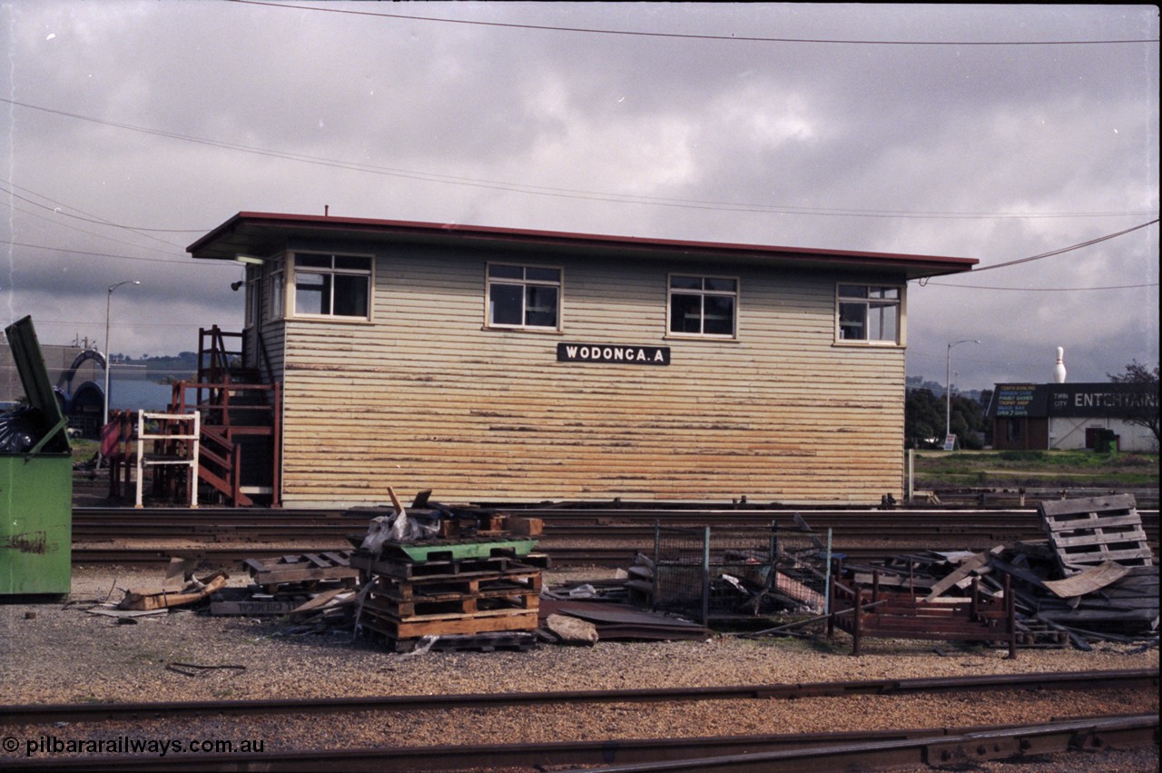142-2-23
Wodonga station yard, signal box A, front elevation, load of pallets and rubbish in shot, staff exchange platform at the left of signal box.
