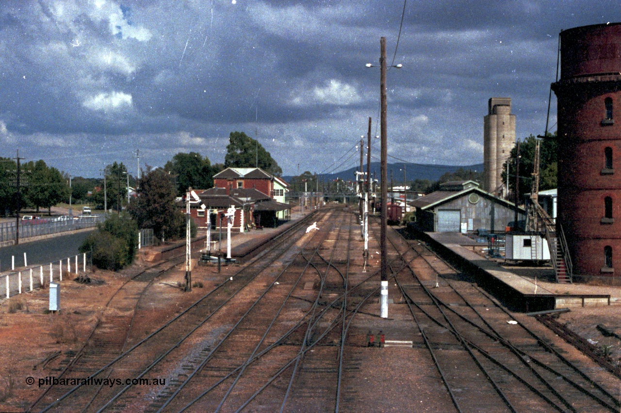 143-01
Wangaratta station yard overview looking south from footbridge, the broad gauge down Wahgunyah Special mixed train 'Stringybark Express' arrives and the signal man swaps electric staffs with the crew, the 18th century infrastructure clearly on display here, semaphore signal Post 20 is pulled off for departure, station building and platform, elevated signal box, signal posts and interlocking, goods shed and water tower.
