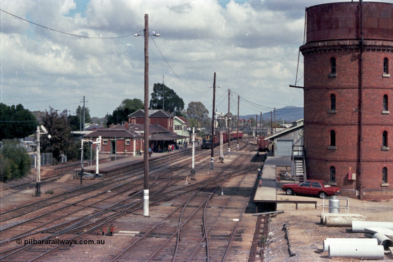 143-03
Wangaratta station yard overview looking south from footbridge, VR liveried Y class Y 133 Clyde Engineering EMD model G6B serial 65-399 brings the board gauge down Wahgunyah Special 'Stringybark Express' to a stop at the platform, the fully interlocked yard and 18th century infrastructure clearly on display here, semaphore signal Post 20 is pulled off for departure, station building and platform, elevated signal box, signal posts and interlocking, goods shed and water tower.
