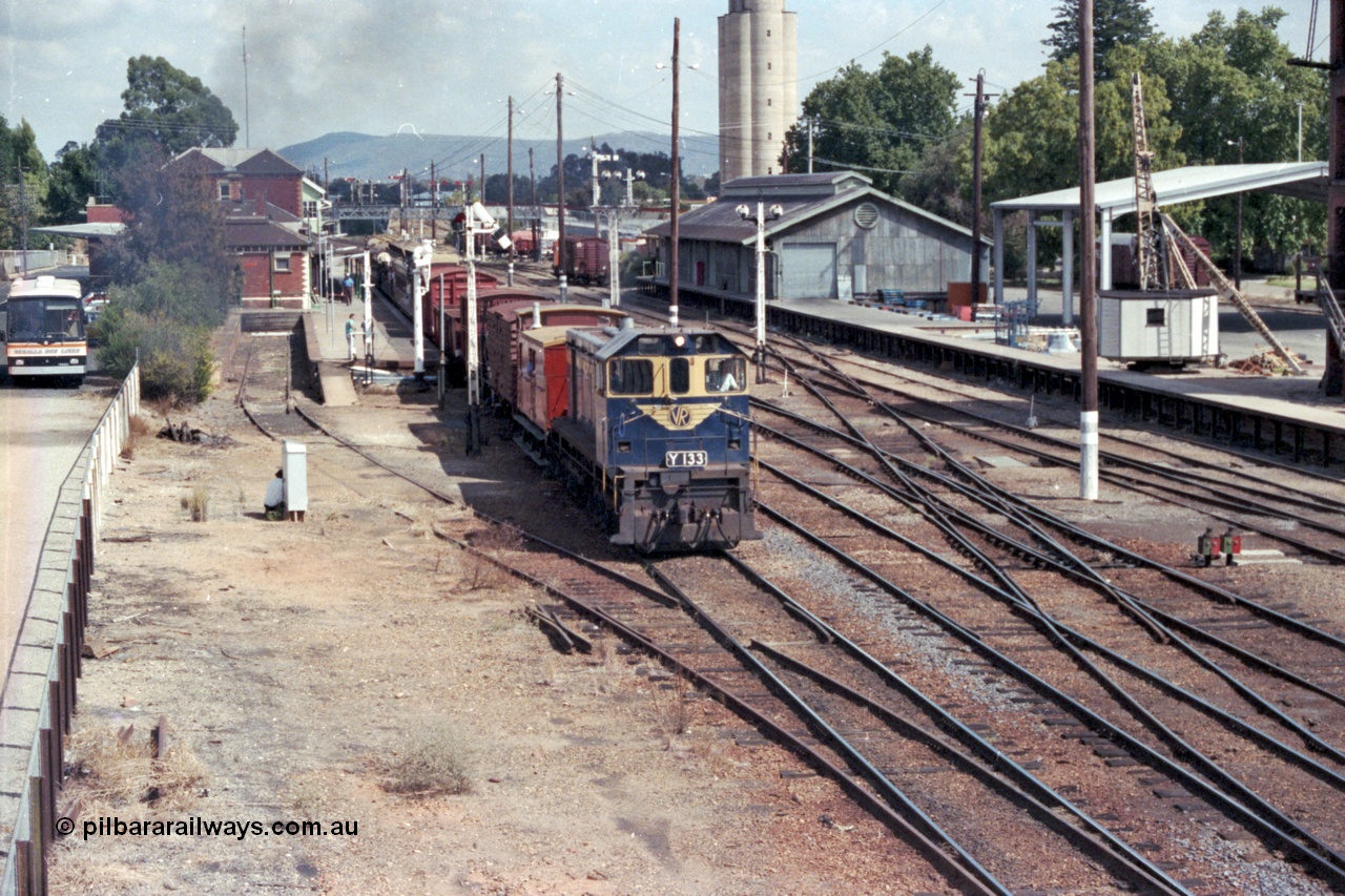 143-06
Wangaratta station yard overview looking south from footbridge, VR liveried Y class Y 133 Clyde Engineering EMD model G6B serial 65-399 departs the platform in the still fully interlocked yard with the broad gauge down 'Stringybark Express' mixed train to Wahgunyah, the K crossing for Siding A having only recently removed, signal post, goods shed, silos and yard crane.
Keywords: Y-class;Y133;Clyde-Engineering-Granville-NSW;EMD;G6B;65-399;
