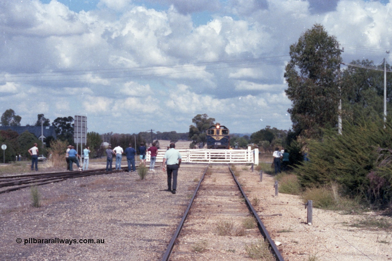 143-19
Rutherglen yard view, the signaller walks down to the hand operated swing gates protecting Howlong St to allow broad gauge VR liveried Y class Y 133 Clyde Engineering EMD model G6B serial 65-399 to cross with the down Wahgunyah mixed 'Stringybark Express' special.
