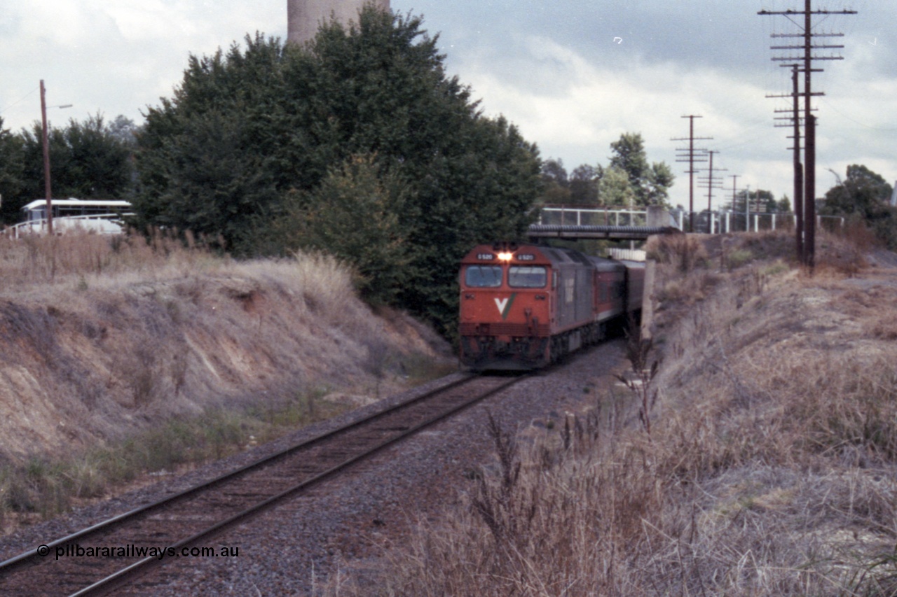 148-30
Wangaratta, V/Line standard gauge G class G 520 Clyde Engineering EMD model JT26C-2SS serial 85-1233 leads the down Inter-Capital Daylight under the station access bridge with town water tower behind bushes, broad gauge yard and station is to the right of image.
