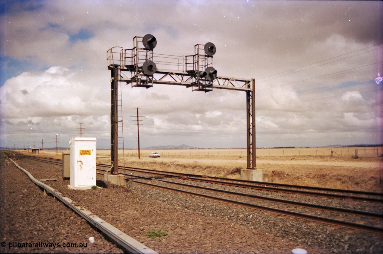 153-1-05
Bank Box Loop signal gantry at the east end, looking towards Bacchus Marsh, relay room in the background, train control phone booth next to gantry, searchlight up home signals 10 for mainline departure and 12 for loop departure.
