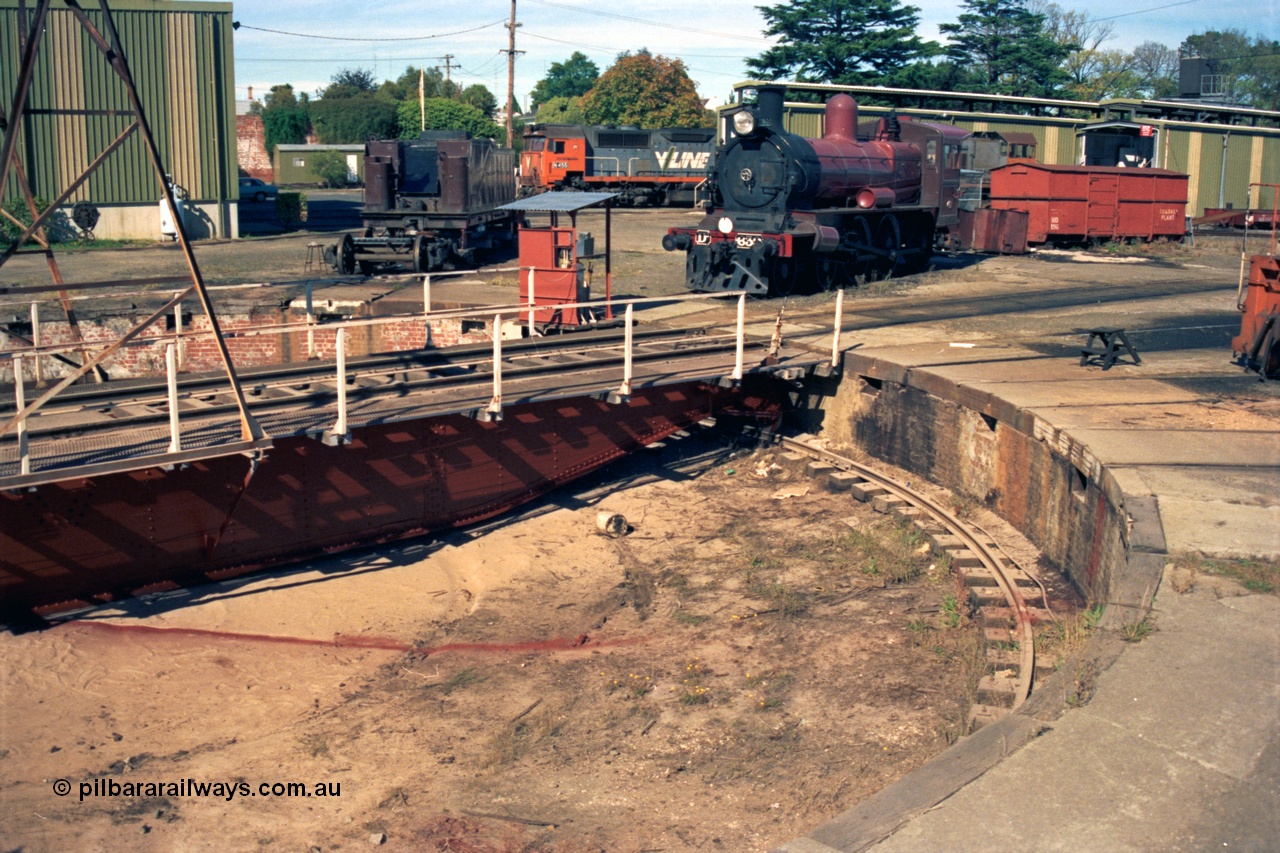 153-2-10
Ballarat East loco depot turntable and pit, shows freshly painted frame, D3 639 renumbered from 658 undergoing rebuild, V/Line broad gauge N class N 455 'City of Swan Hill' Clyde Engineering EMD model JT22HC-2 serial 85-1223 obscured Y class Y 165 Clyde Engineering EMD model G6B serial 68-585, grounded four wheel HD type waggon HD 196 'Gradall Plant'.

