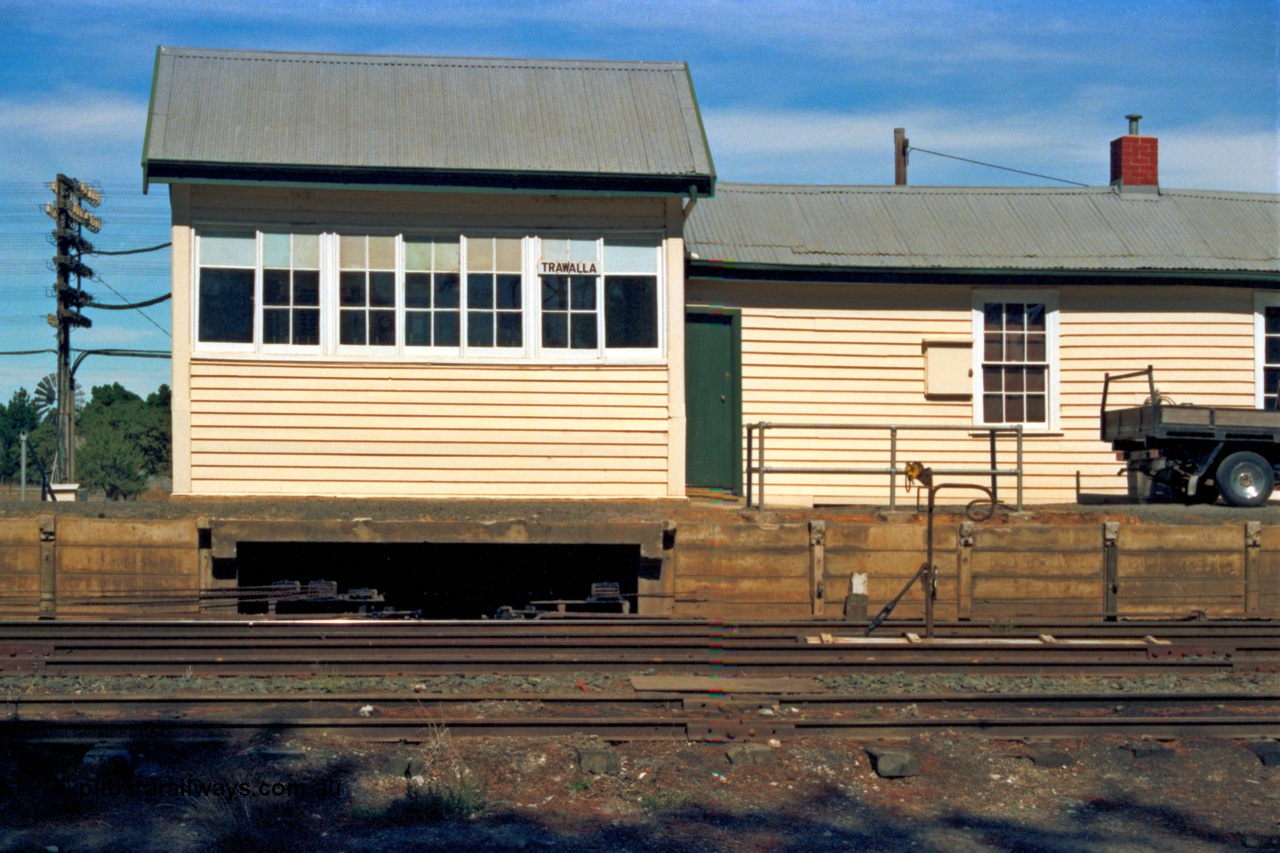 153-2-20
Trawalla signal box and automatic electric staff exchange apparatus setup with staff for an up train, point rodding and signal wires leaving the platform, levers visible in windows.
