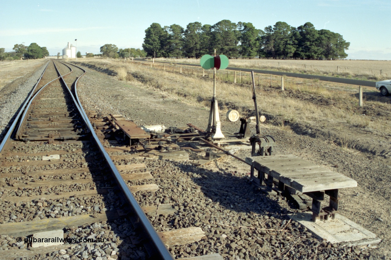 153-3-06
Tatyoon station yard overview from Ararat end, shows trailable points lever and indicator, goods shed and Murphy silos visible in the background.
