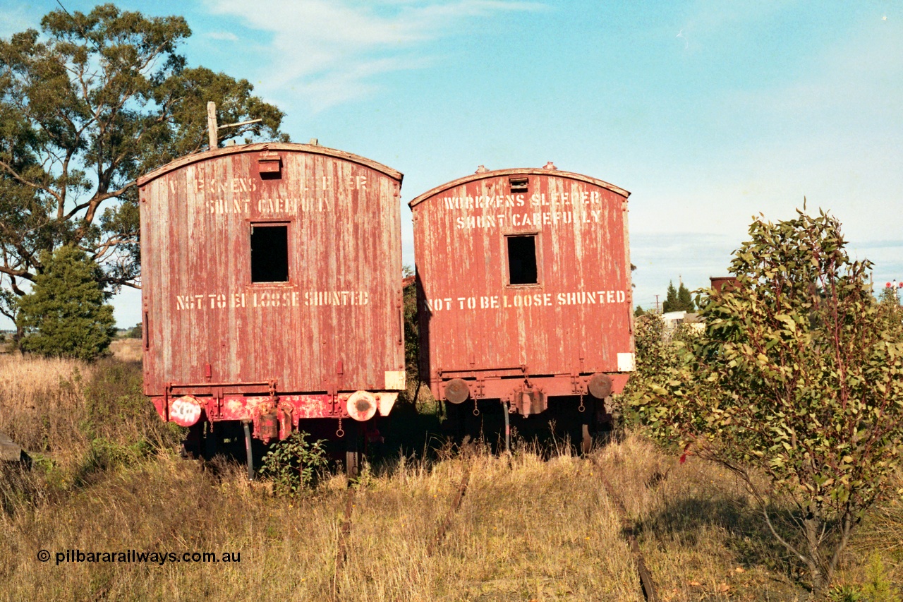 155-11
Wallan, stored 'OFF REG' waggon awaiting scrapping, bogie Ways and Works workmen's sleeper waggons, end view shows coupler, buffers and signage, the water tank can be seen behind the tree at right and the double disc signal post 15 at extreme right.
