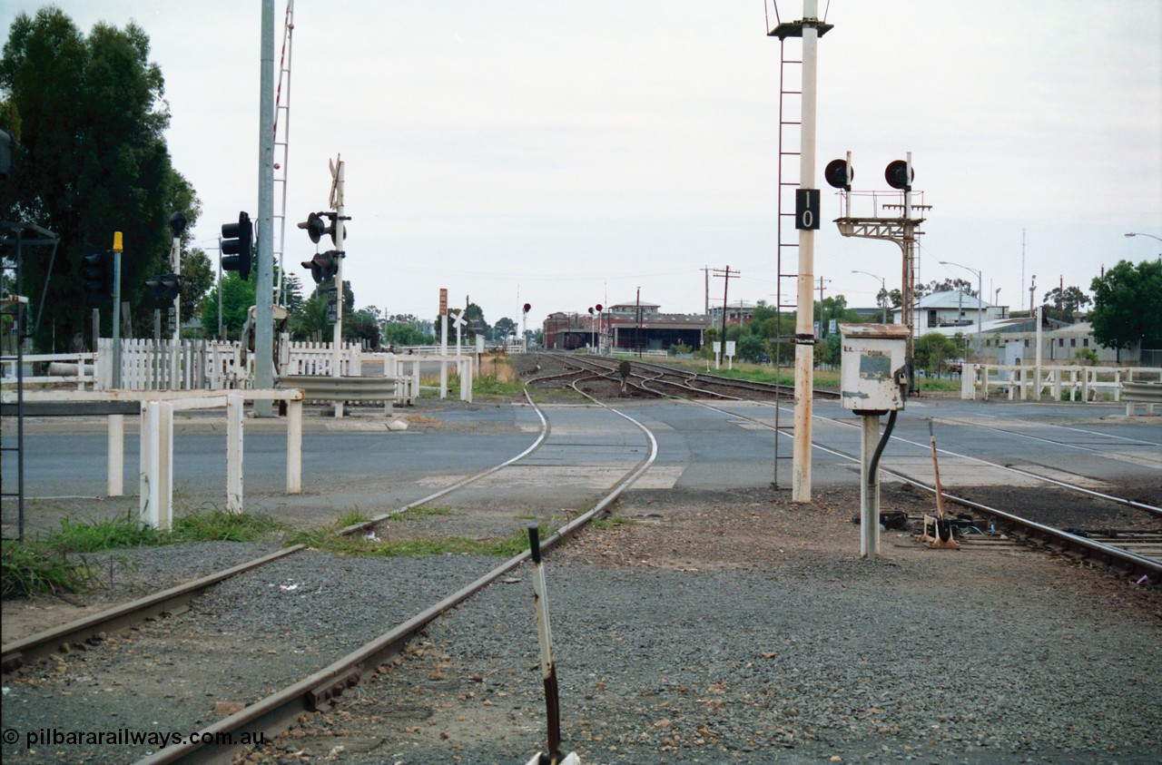 156-11
Shepparton station yard view looking north across High Street grade crossing, dwarf signal 8 just across road, SPC Siding and building in the background, searchlight signals in the distance are up and down home signals at Fryers Road grade crossing, down home signal post 10 and up home signal post 12, point lever, electric interlocking and phone cabinet.
