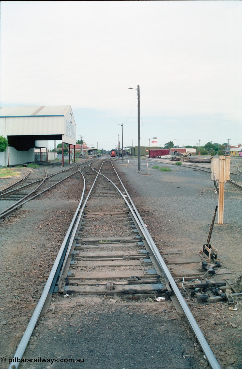 156-12
Shepparton station yard overview, looking south from High Street, mainline points from the Tocumwal line set for No.1 or platform Road, showing point lever, interlocking and telephone cabinet, line on the left is to Katamatite, now Dookie and the former Engine Track heading into the Tubemakers awning, yard roads, goods shed, Freightgate and cement silos in the background right hand side.
