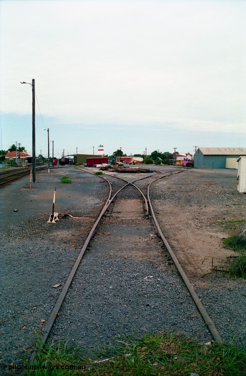 156-13
Shepparton station yard overview looking south at the No.5 Road points and lever towards the goods shed and stabled T class, fuel train and louvre vans, the former Fruit Siding curves around the back of the goods shed at right, grounded B van and per way stockpiles of rails and pipes in middle of frame, station building and platform on the left.
