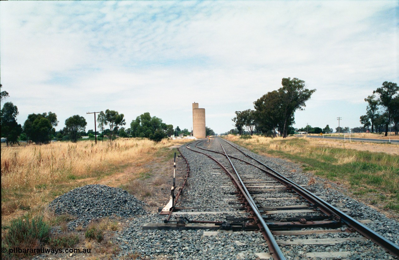 156-19
Tallygaroopna, station yard overview looking south, mainline points for siding with lever and staff lock interlocking, point rodding for derail, Williamstown style silo complex.
