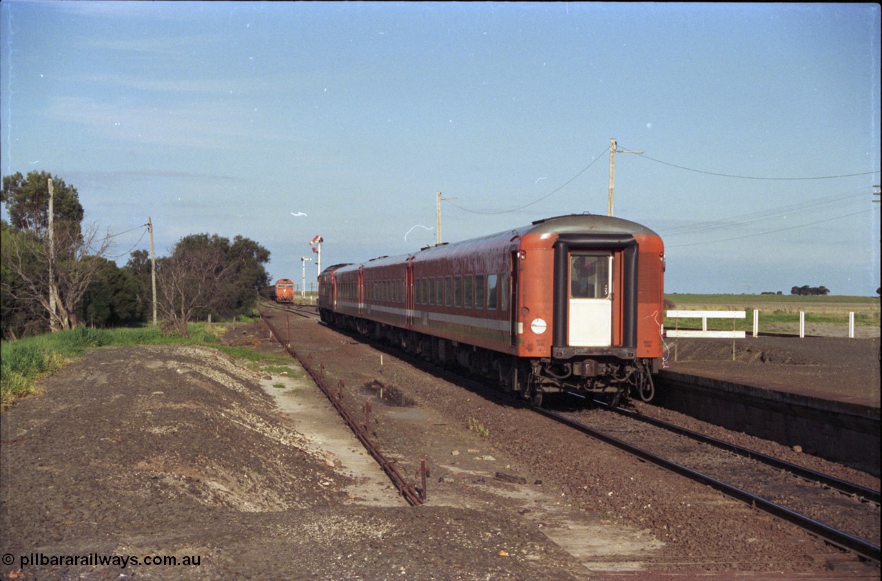 157-02
Gheringhap, station view looking east from former up platform, V/Line broad gauge A class A 77 Clyde Engineering EMD model AAT22C-2R serial 83-1181 rebuilt from B 77 Clyde Engineering EMD model ML2 serial ML2-18 leads the up Ararat to Melbourne via Nth Geelong passenger train with a three car N set, along the mainline heading now for North Geelong, a down grain train 9121 sits in Siding A, station platform, point rodding and semaphore signals.

