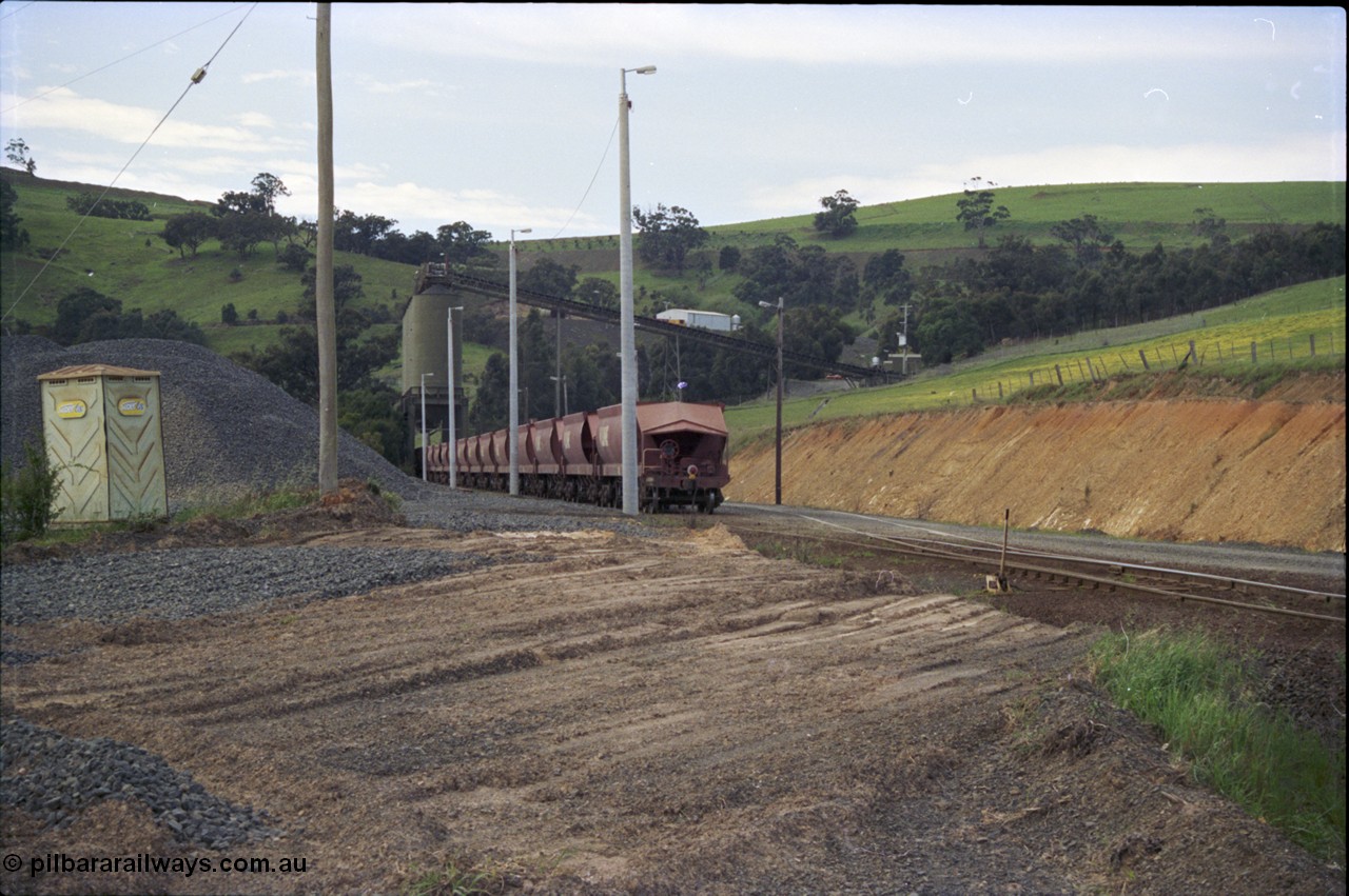157-07
Kilmore East, Apex Quarry Siding, empty broad gauge V/Line stone train rake is under the loading bins having just arrived, locomotives cutting off to shunt round, oversize ballast pile and 'Super Loo' on the left.
