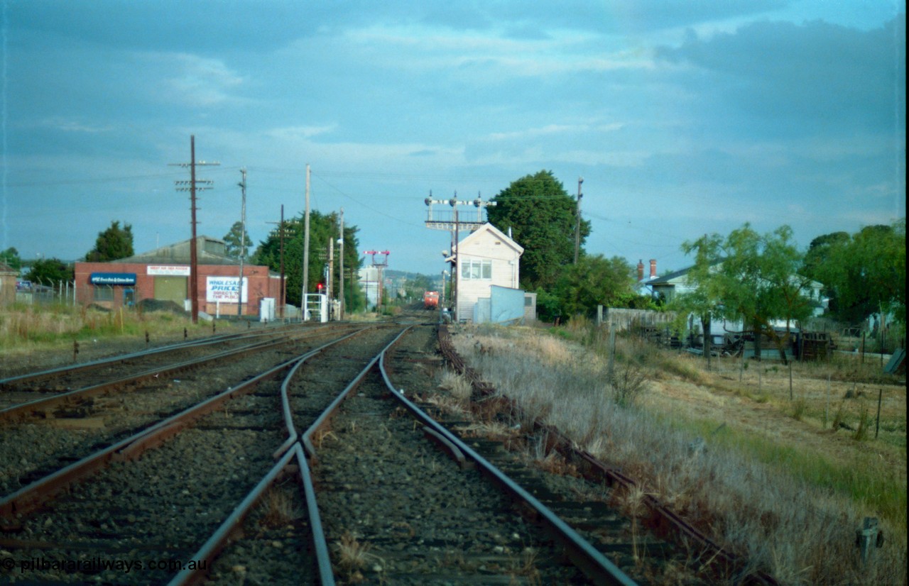 159-17
Ballarat D Signal Box, Linton Junction, broad gauge track view from the Cattle Yard Line looking east, Linton Line then the Ararat Line with the down crossover visible, triple doll semaphore signal 20 facing down train is visible behind the signal box, with the Gillies Street interlocked gates open, staff exchange platform and up home semaphore signal post 19, down home semaphore signal post 18 is visible and pulled off to allow the approaching train to pull up to Gillies Street, points, track work and point rodding.
