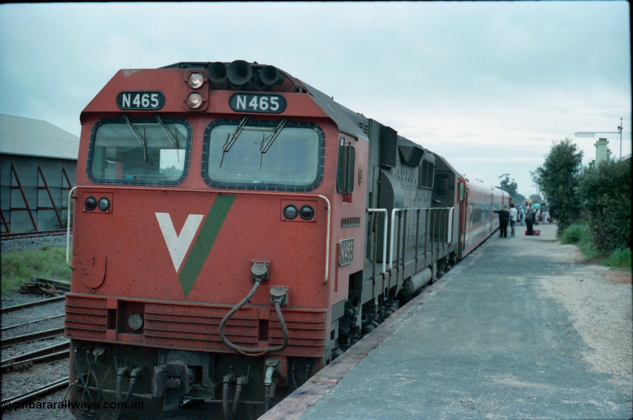 160-09
Murchison East, station platform view of down Cobram passenger train pausing for platform duties behind V/Line broad gauge N class locomotive N 465 'City of Ballaarat' Clyde Engineering EMD model JT22HC-2 serial 86-1194 with N set, super phosphate shed at left of image.
Keywords: N-class;N465;Clyde-Engineering-Somerton-Victoria;EMD;JT22HC-2;86-1194;