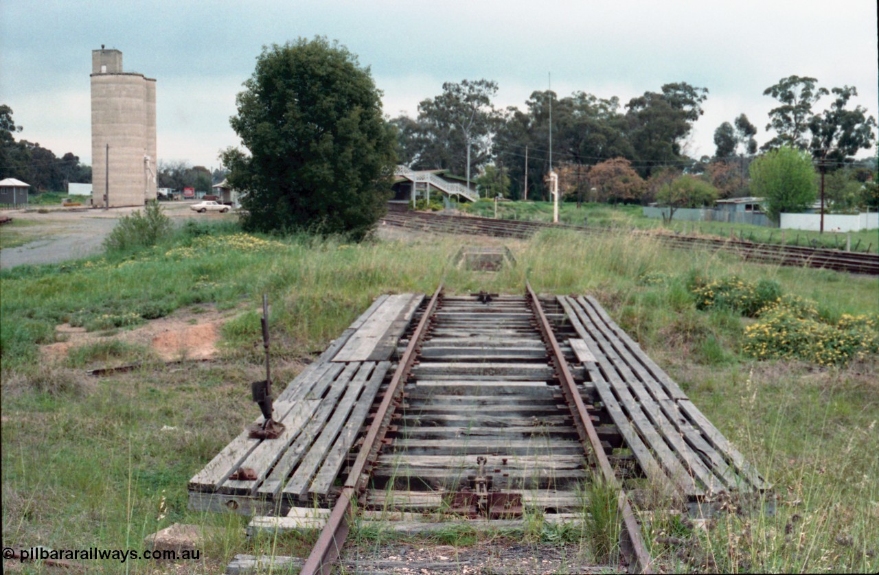 161-07
Numurkah, yard view looking south from turntable track, open deck and pit with locking lever, ash pit visible along with steam era water stand pipe on No.1 Rd, Williamstown style silo complex on the left with goods shed obscured by tree, HK Holden sedan, station building and steel lattice footbridge in the middle of frame.
