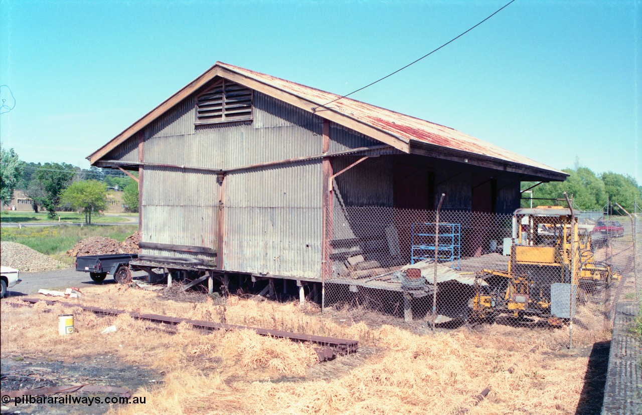 162-1-01
Healesville, view of goods shed, eastern side and loading platform, fenced off compound with track machines, standard Victorian Railways 20 ft goods shed.

