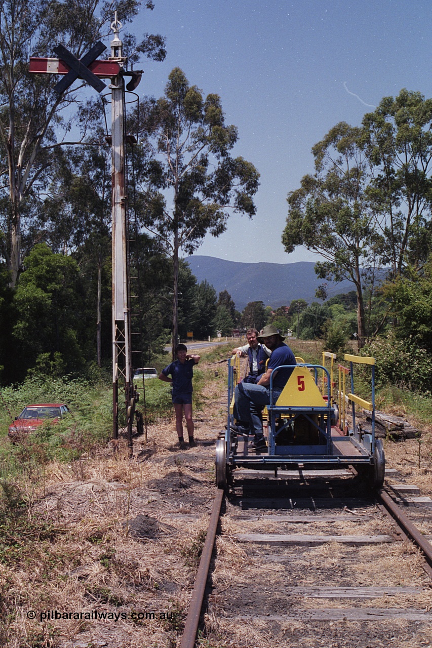 168-19
Healesville, broad gauge ganger's trolley #5 at the down home semaphore signal post with some YVTR volunteers, black cross on semaphore means signal not in use.
