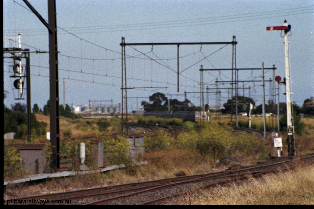 172-02
Sunshine, broad gauge Melbourne metropolitan electric service operated by 'The Met', this up Hitachi 6 car 'spark' or electric train rounds the curve east of Sunshine as it heads to Tottenham, signal post 49 controls up trains on the Sunshine - Newport Loop Line, with the disc controlling access to the GEB sidings, the points facing the camera leads to the main running lines and the Sunshine yard or what remained of it.
