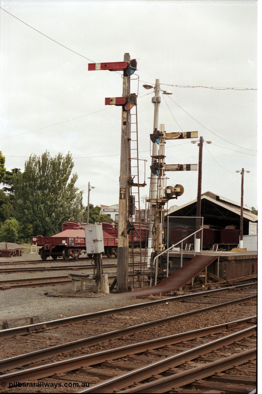 172-37
Ballarat station yard, platform, wooden semaphore signal post 21 facing camera and 21B at platform one facing away, Tait carriages and VZBF class bogie brake block transport waggon in background. Post 21 top is the Down Home No.1 to Post 26, bottom is the Calling On to No. 1. Post 21B top is Up Home No. 1 to Post 7, bottom is Up Home No.1 to No.1 A to Post 9B. Left disc is No.1 to Goods Line via 'Z' to Post 7. Right disc is from No.1 to Loco Track Post 10 or Goods Track 'R'.
