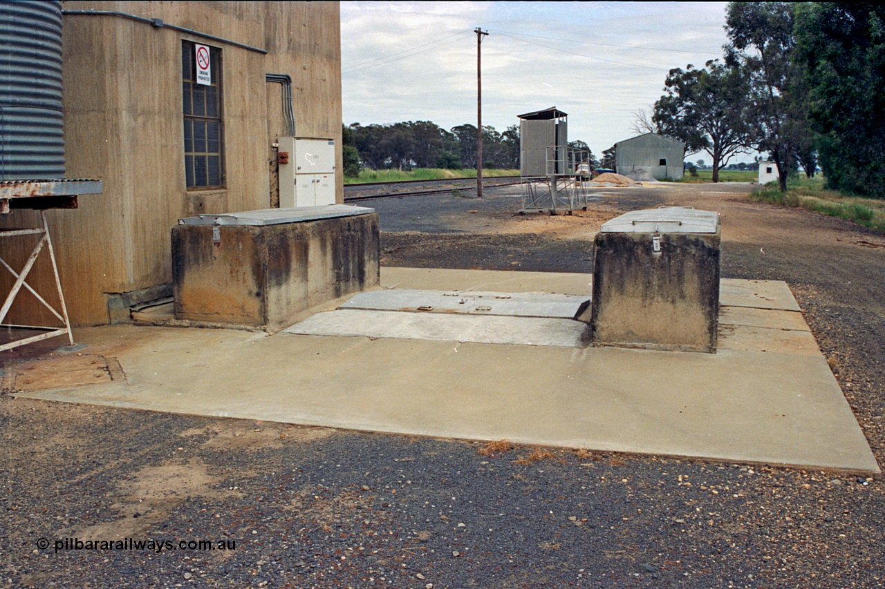 175-23
Pine Lodge, view of road receival point, or truck unloading dump point for a Williamstown style silo complex, GEB sampling gantry, with super phosphate shed in the background, road vehicle weighbridge visible on the right.
