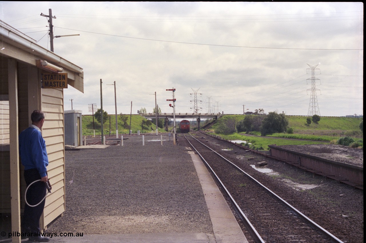 179-09
Gheringhap, station yard view looking west from the station building as the signaller stand by with an electric staff in a hoop as he prepares to swap staves with down loaded grain train 9122 coming off the Ballarat line behind a pair of V/Line G class locomotives led by G 515 Clyde Engineering EMD model JT26C-2SS serial 85-1243, the Midland Highway overpass frames the train with signal post 4. The former up platform is visible on the right and the pit where the removed double mainline used to be is clearly visible.
Keywords: G-class;G515;Clyde-Engineering-Rosewater-SA;EMD;JT26C-2SS;85-1243;