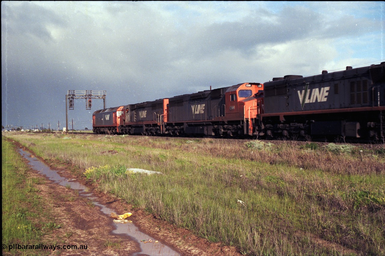 183-03
Deer Park West, an up broad gauge V/Line goods train behind the quad lash up of a G class, 2 C classes and an X class as they pass under signal gantry with searchlight signals 1/10 and 1/22 on the North Line.
