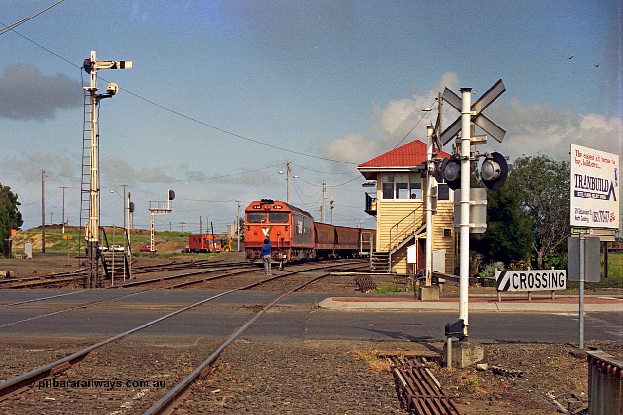 185-05
North Geelong C Box looking across the Separation Street grade crossing as a V/Line G class locomotive G 514 Clyde Engineering EMD model JT26C-2SS serial 85-1242 departs North Geelong Yard with 9121 empty grain train, the signaller has the Gheringhap electric staff offered up to the driver, the tracks to the grain loop and the Loop Line to Melbourne are curving around to the left beyond the mechanical and electric signal posts.
Keywords: G-class;G514;Clyde-Engineering-Rosewater-SA;EMD;JT26C-2SS;85-1242;