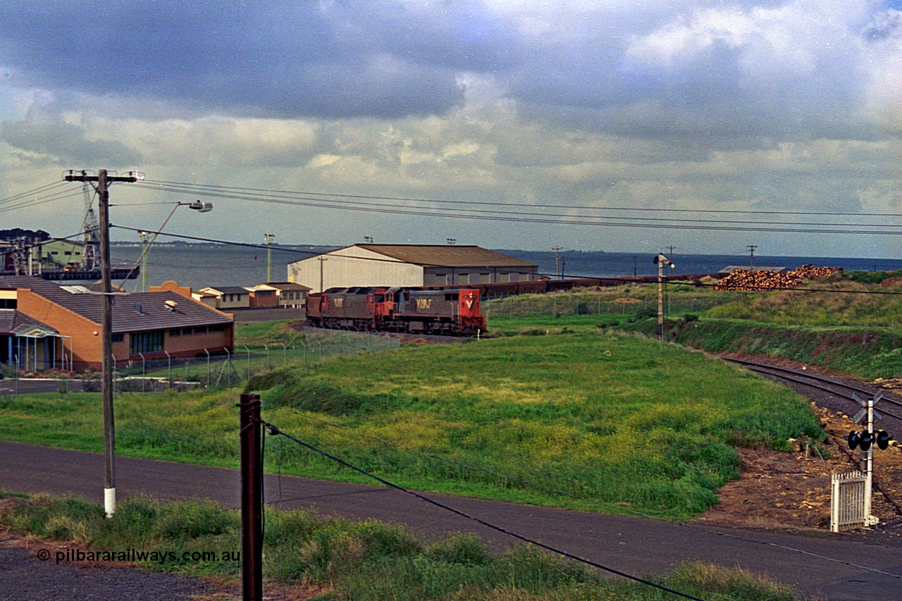 185-09
North Geelong Grain Loop view from Corio Quay Road across to Corio Quay with Access Road and grade crossing, and the former tracks to South Quay visible at the left corner, the grain train is approaching the Home Signal that protected the former Freezing Works Siding.
