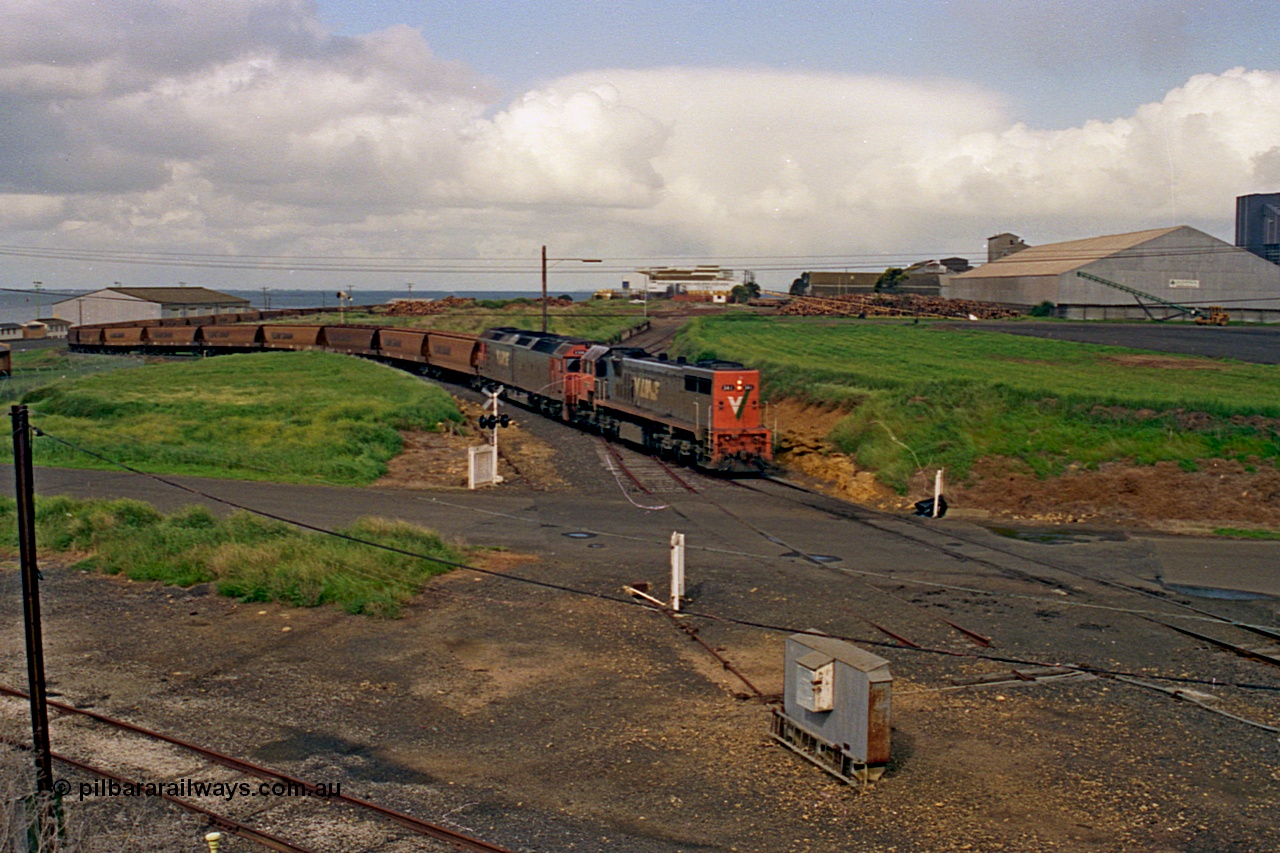 185-11
North Geelong Grain Loop view from Corio Quay Road across Access Road grade crossing with the tracks to Corio Quay at the very bottom of image, as the grain train behind V/Line locos X class locomotive X 41 Clyde Engineering EMD model G26C serial 70-704 long end leading and G class locomotive G 528 Clyde Engineering EMD model JT26C-2SS serial 88-1258 having past the Home Signal and crossing the former tracks for the Freezing Works Sidings.
Keywords: X-class;X41;Clyde-Engineering-Granville-NSW;EMD;G26C;70-704;